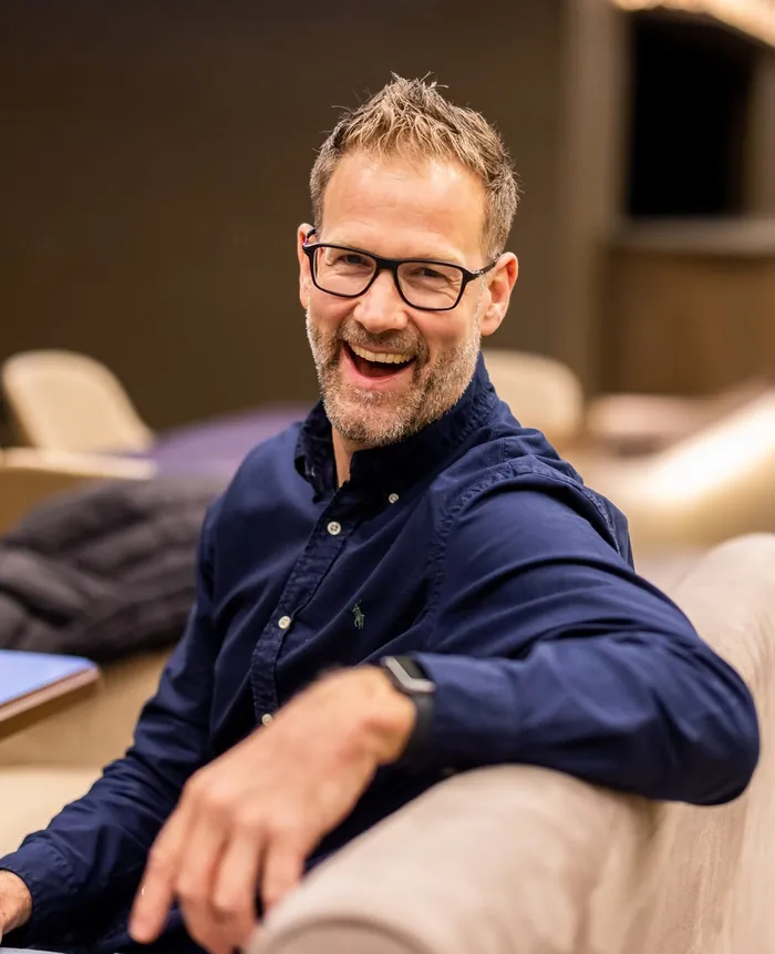 Christian Bischoff lacht, auf einem Sofa sitzend